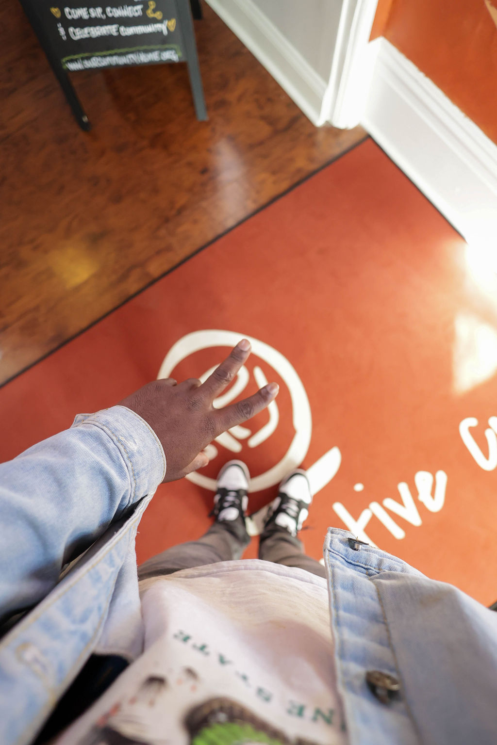 A peace sign over the branded entrance mat beside a chalkboard reading Come Sip, Connect & Celebrate community