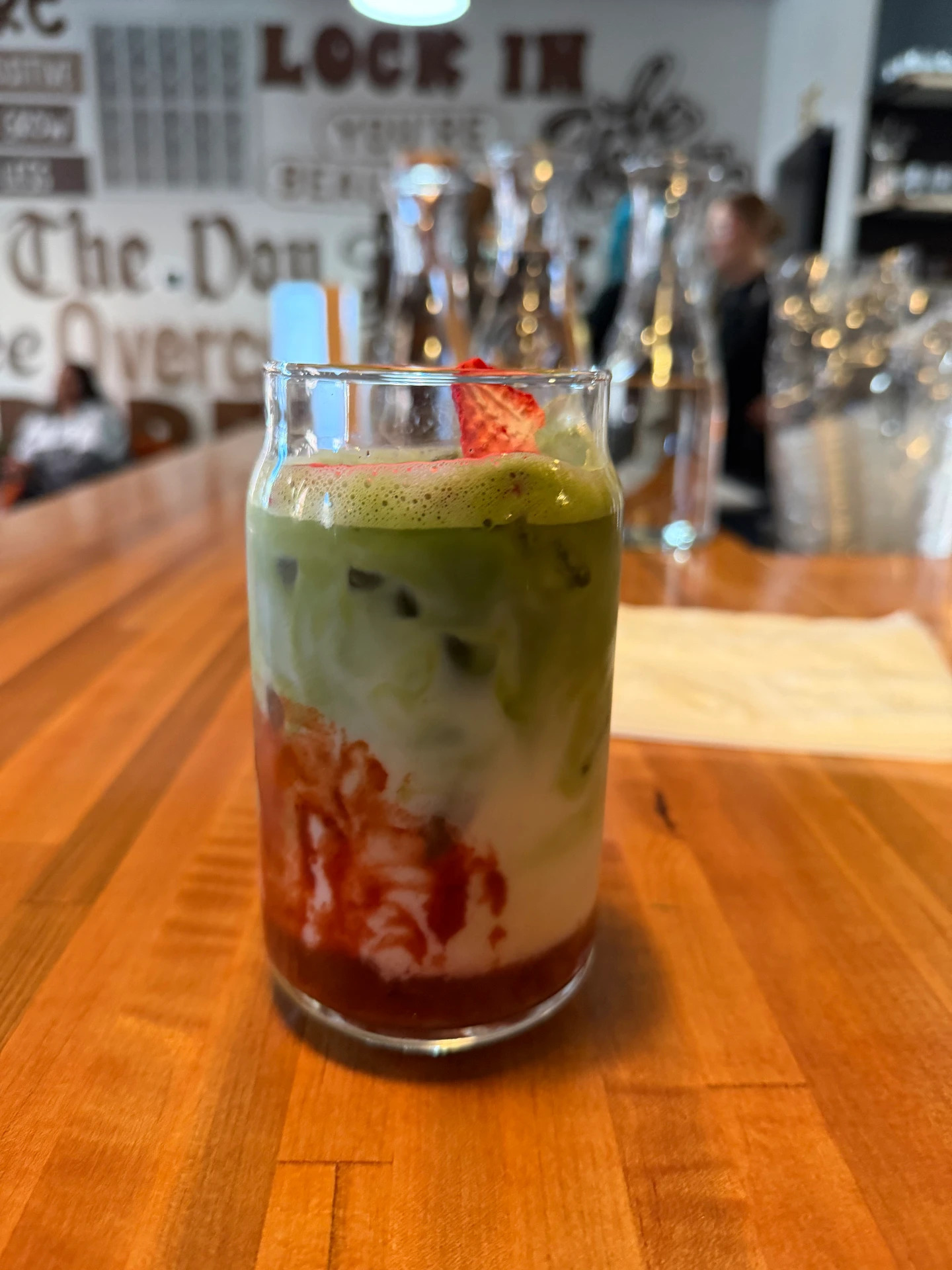 An iced strawberry matcha latte garnished with a dried strawberry slice at the counter